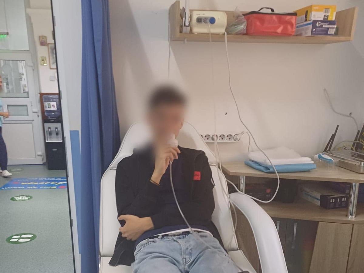Pacient așezat în fotoliu, respirând prin piesa bucală a nebulizatorului de pe raft