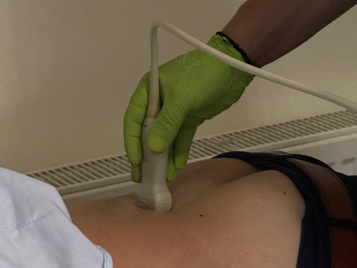 Mâna medicului, în mănușă, ține sonda ecografului pe spatele unui pacient