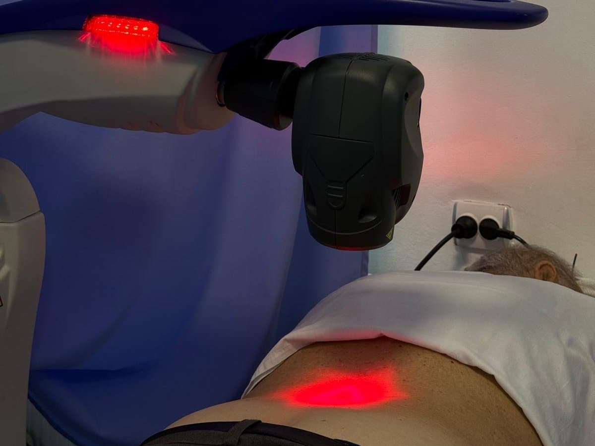 Ședință de terapie cu laser MLS: aparatul luminează zona lombară a unui pacient întins pe pat