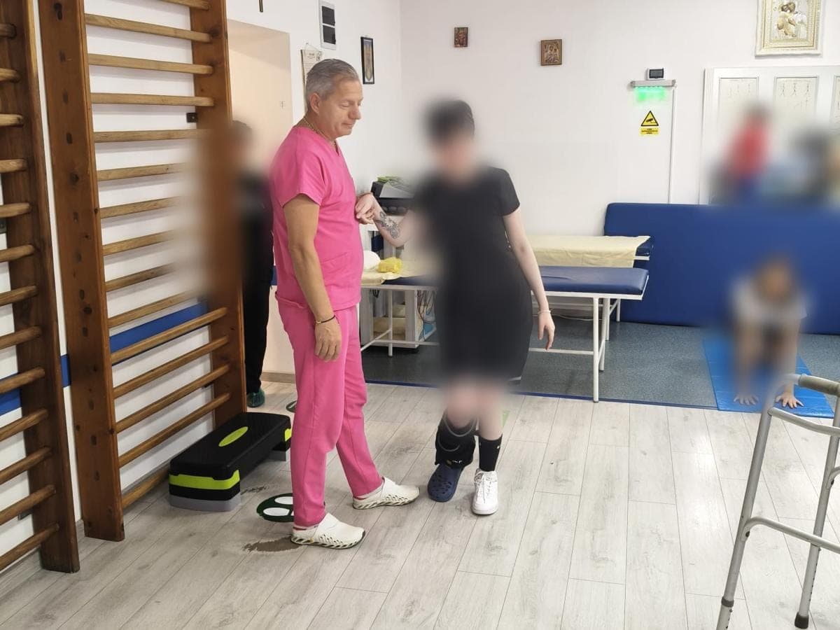 Medicul o ține de braț pe o pacientă la exercițiile de mers, în sala de recuperare