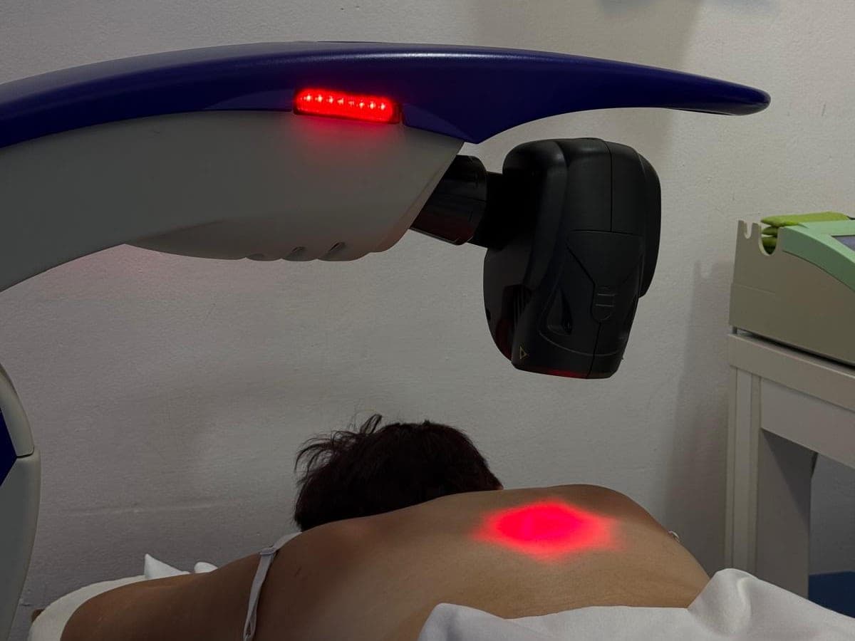 Aparatul laser MLS deasupra unei paciente întinse pe pat, cu lumina roșie pe spate