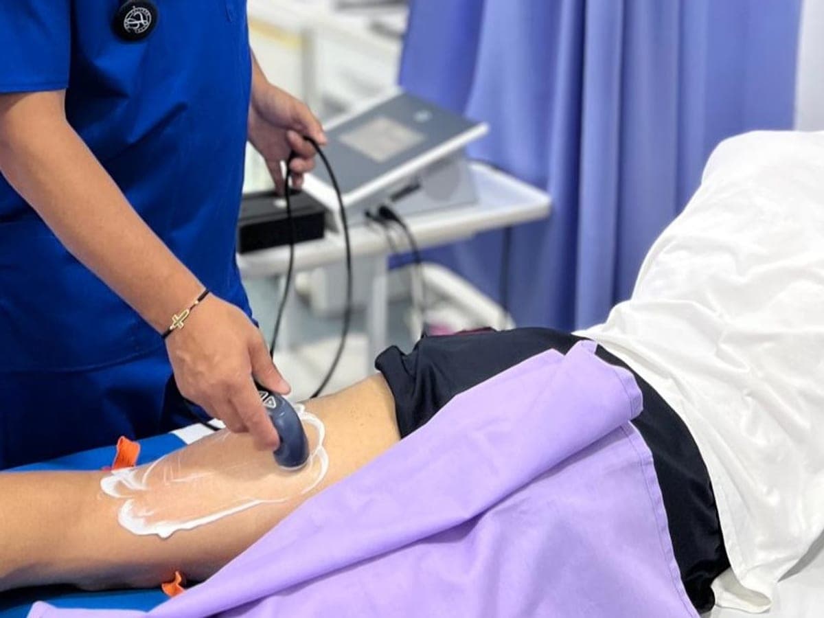 Mâna terapeutului trece aplicatorul TECAR peste gamba unui pacient întins pe pat